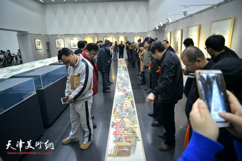 来宾在画展现场观赏刘维仑的《盛世集贸图》和《盛世闹春图》长卷。